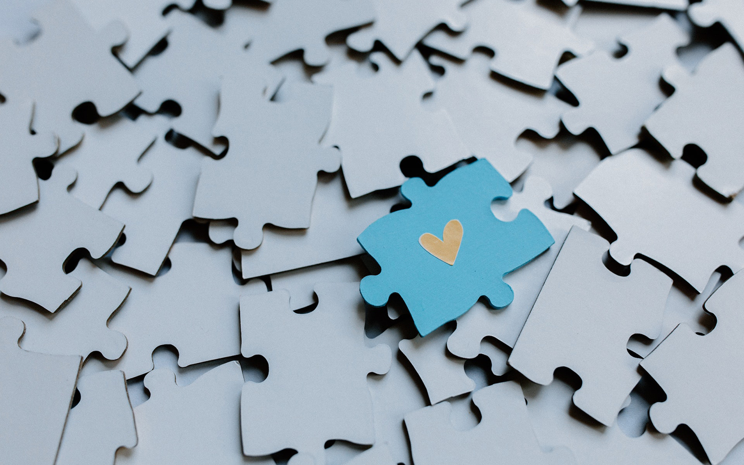 a blue puzzle piece with a heart atop a pile of lighter blue puzzle pieces